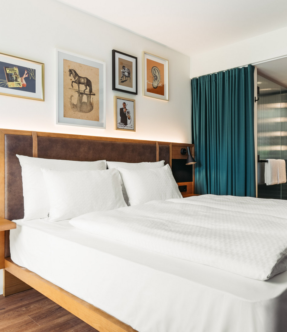 Double bed with white bed linen next to a green curtain and an open bathroom 
